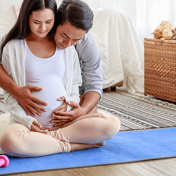 Pregnant woman sitting on an exercise mat with her partner holding her belly, illustrating pregnancy wellness for The Advanced Spine Center in New Jersey