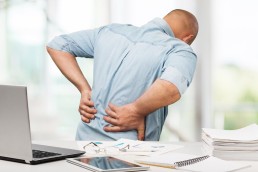 man holding back in pain while next to desk