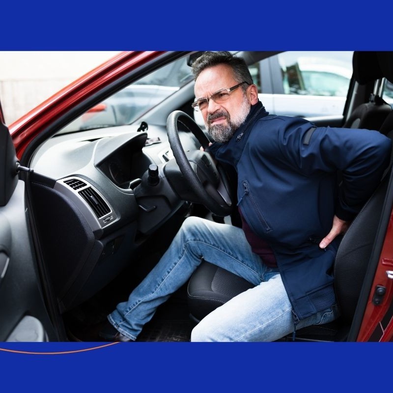 Man holding his lower back while seated in a car, illustrating back pain treated at The Advanced Spine Center in New Jersey.