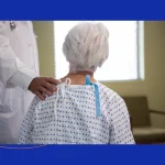 Elderly patient in a hospital gown meeting with a spine surgeon at The Advanced Spine Center in New Jersey.